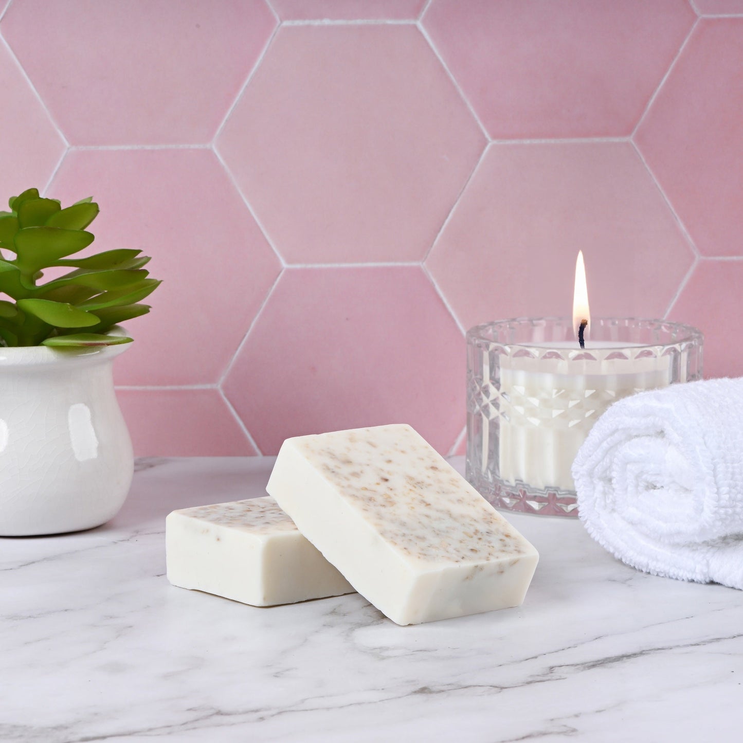 Handmade oatmeal soap bars on marble with candle and plant for skincare.