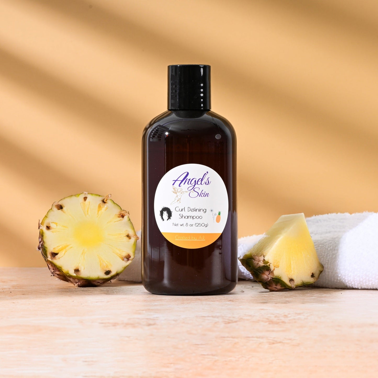Bottle of Angel's Skin Curl Defining Shampoo with pineapple slices and a towel on wooden surface