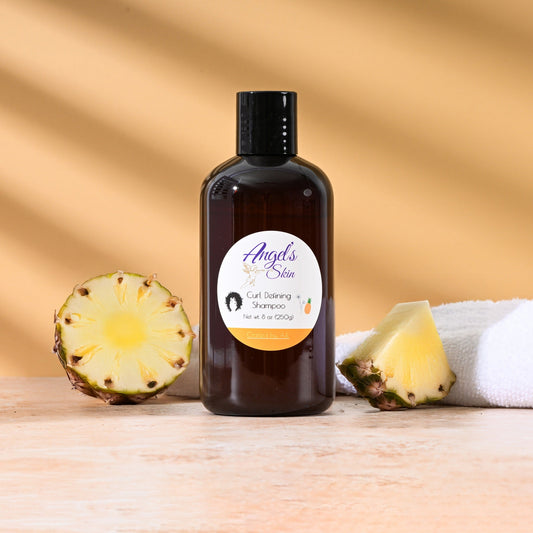 Bottle of Angel's Skin Curl Defining Shampoo with pineapple slices and a towel on wooden surface